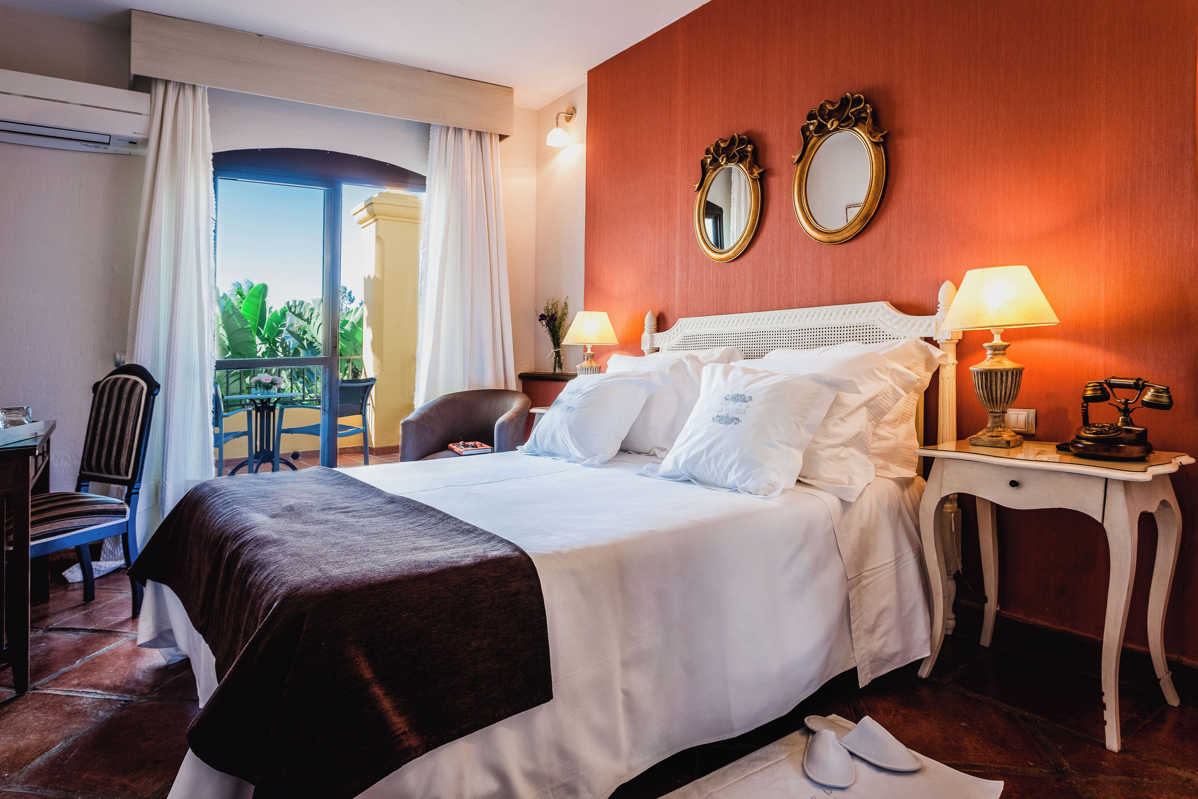 Habitación de hotel con cama, dos mesitas de noche con lámparas, una silla, un escritorio y una ventana con cortinas.