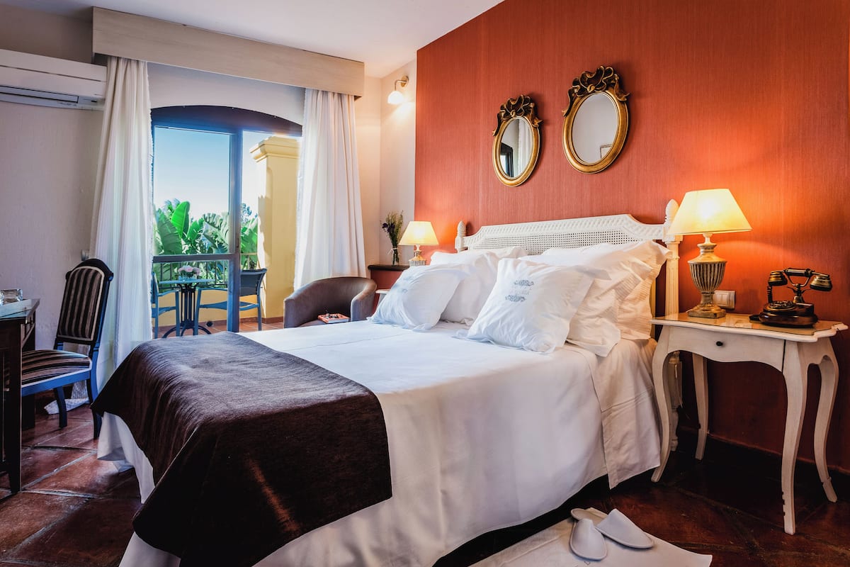 Habitación de hotel con cama, dos mesitas de noche con lámparas, una silla, un escritorio y una ventana con cortinas.