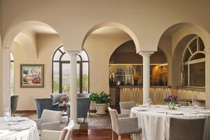 Comedor con mesas redondas, sillas y una planta grande en maceta.