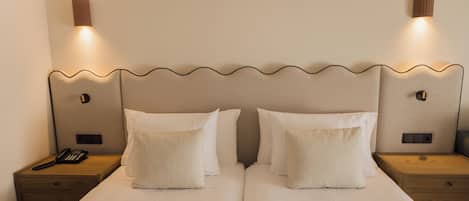 A double bed with two pillows, a nightstand with a telephone, and two wall-mounted light fixtures.