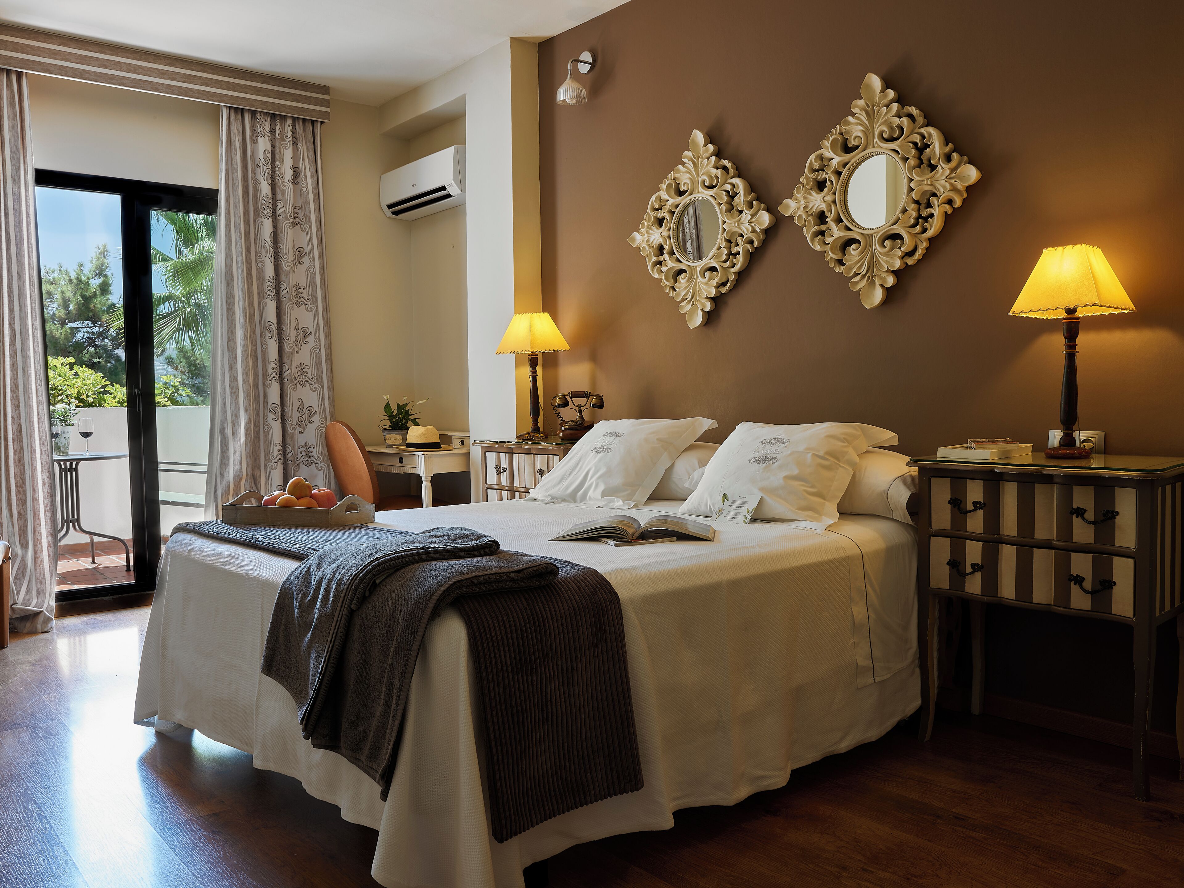 Una habitación de hotel con cama, lámparas de noche, mesita de noche y vistas a través de una ventana.