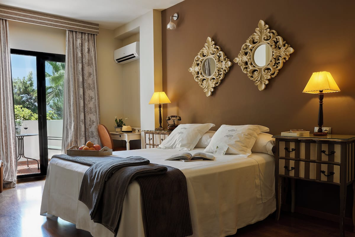 Una habitación de hotel con cama, lámparas de noche, mesita de noche y vistas a través de una ventana.