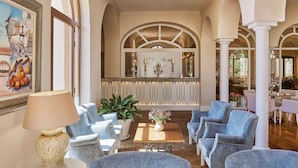 En rummelig lobby med hvælvede lofter, et centralt siddeområde med blå polstrede stole, et sofabord med en vase med blomster og et indramet kunstværk på væggen.