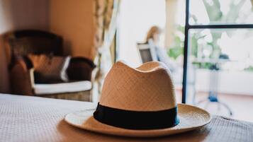 Un sombrero de paja con una banda negra sobre una mesa en una habitación con vistas a una persona sentada a otra mesa al fondo.