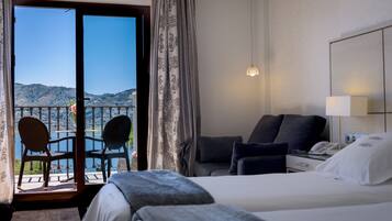 A hotel room with a bed, a desk, a chair, and a view of the mountains through the balcony doors.