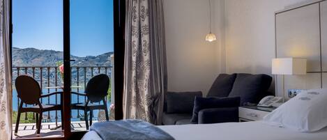 A hotel room with a bed, a desk, a chair, and a view of the mountains through the balcony doors.