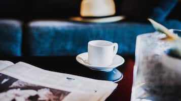 A white cup on a saucer, a glass with a straw, and an open book on a table.