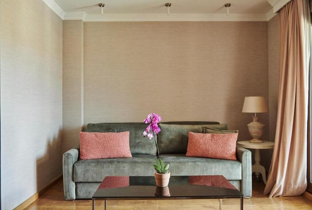 Una sala de estar con un sofá gris, dos cojines rosados, una mesa con una orquídea en maceta y una lámpara en una mesita auxiliar.