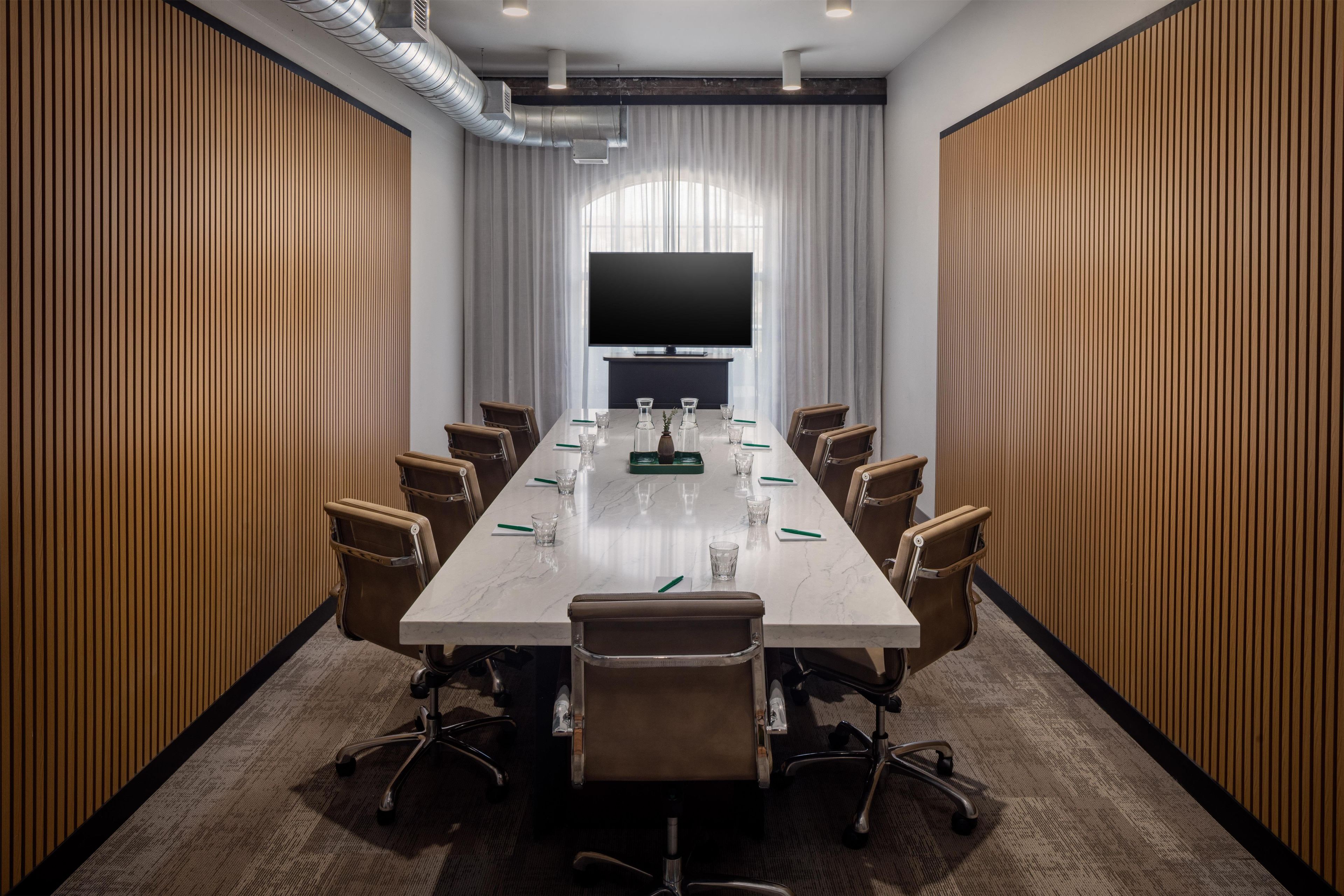 Un salón de conferencias con una larga mesa, sillas, un televisor de pantalla plana grande y paredes de paneles de madera.