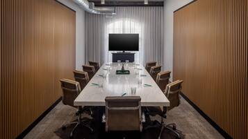 Un salón de conferencias con una larga mesa, sillas, un televisor de pantalla plana grande y paredes de paneles de madera.