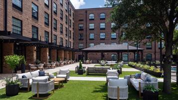 Un patio con mesas al aire libre, un edificio de ladrillo y una piscina.