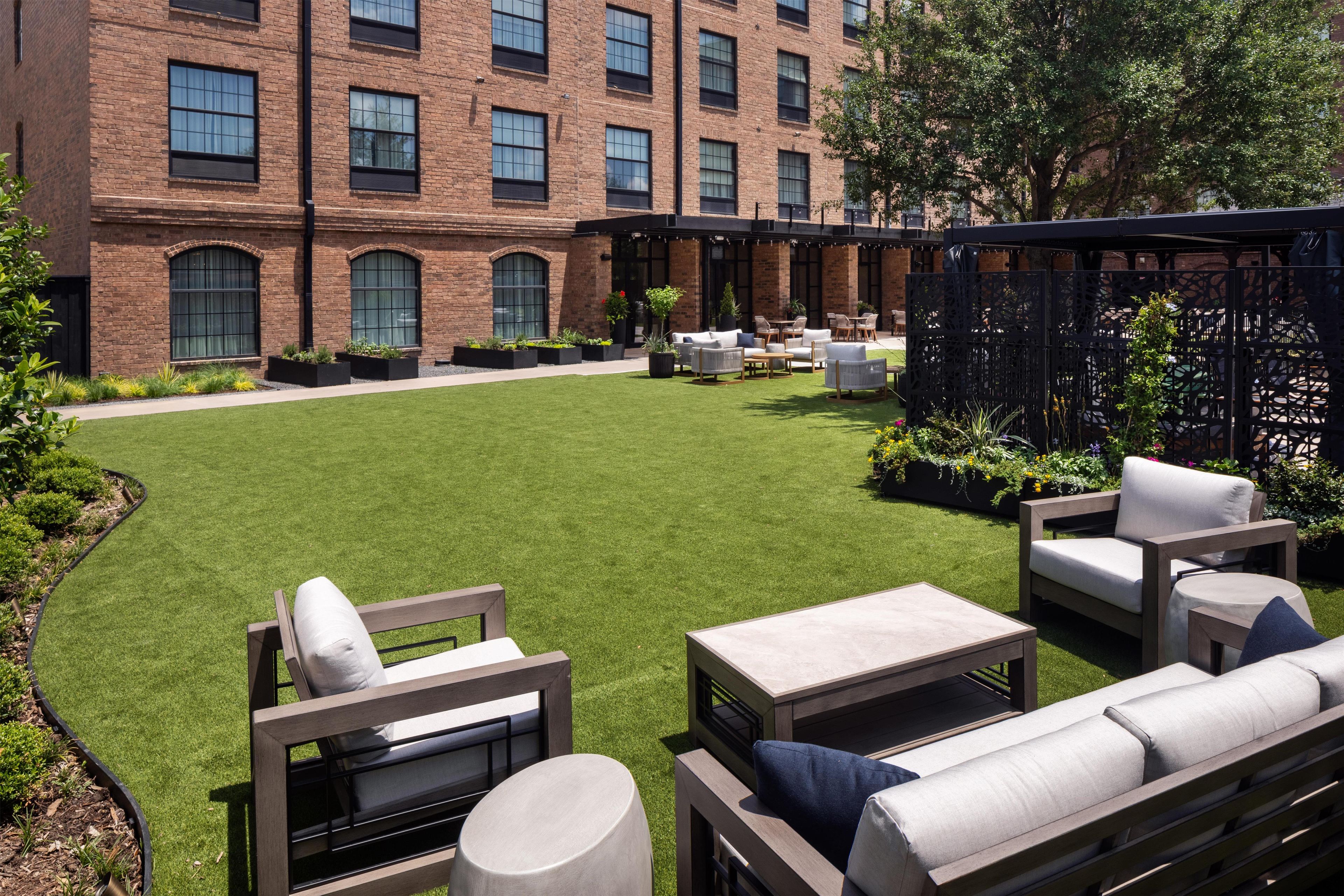 A courtyard with outdoor seating, a brick building, and a garden.