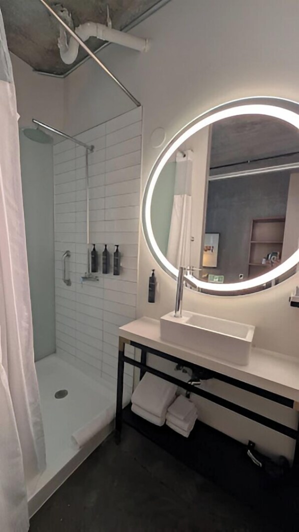 Ein modernes Badezimmer mit einer bodengleichen Dusche, einem runden Spiegel und einem Waschtisch.