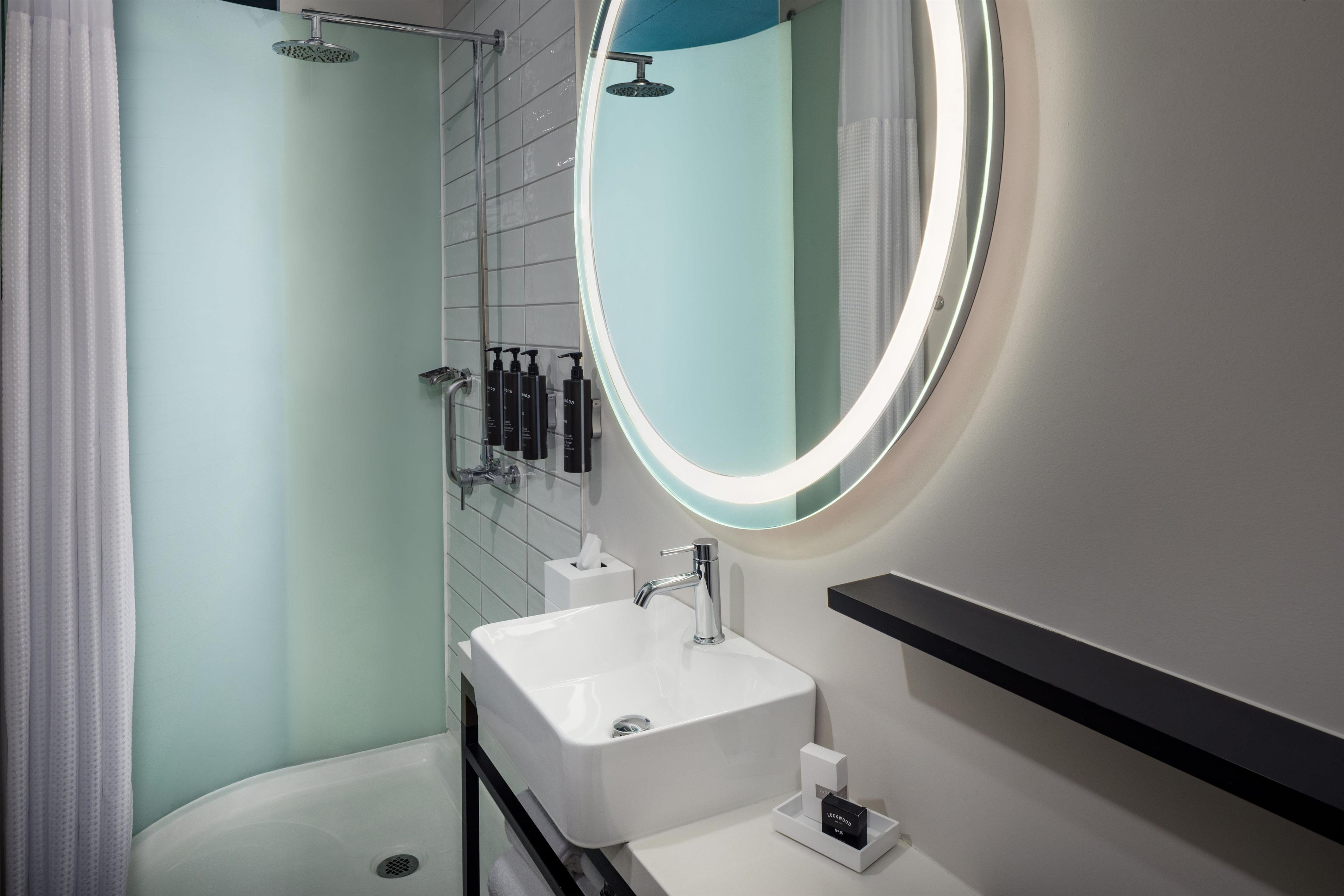 A modern bathroom with a white sink, a round mirror, and a shower.