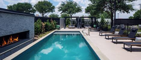 A rectangular pool with a fire feature on one side, surrounded by lounge chairs and a covered seating area.
