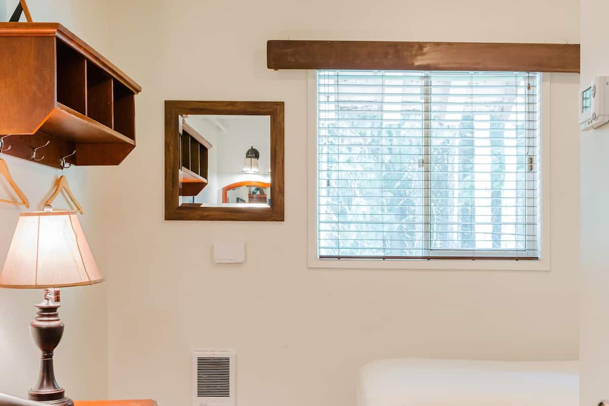 Habitación de hotel con cama, una silla, lámpara, ventana con persianas y un espejo en la pared.