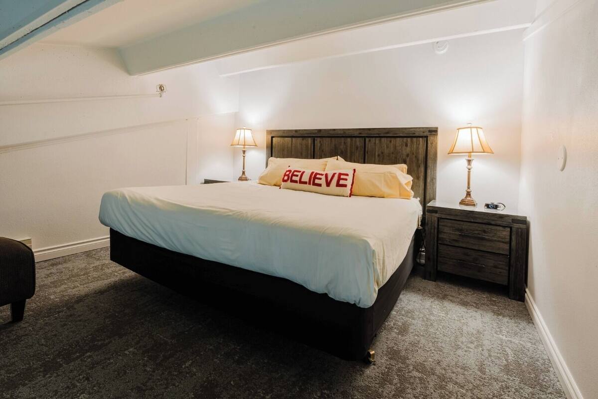 Un dormitorio ordenado con cama, dos lámparas de noche, una mesita de noche y un reloj de pared.