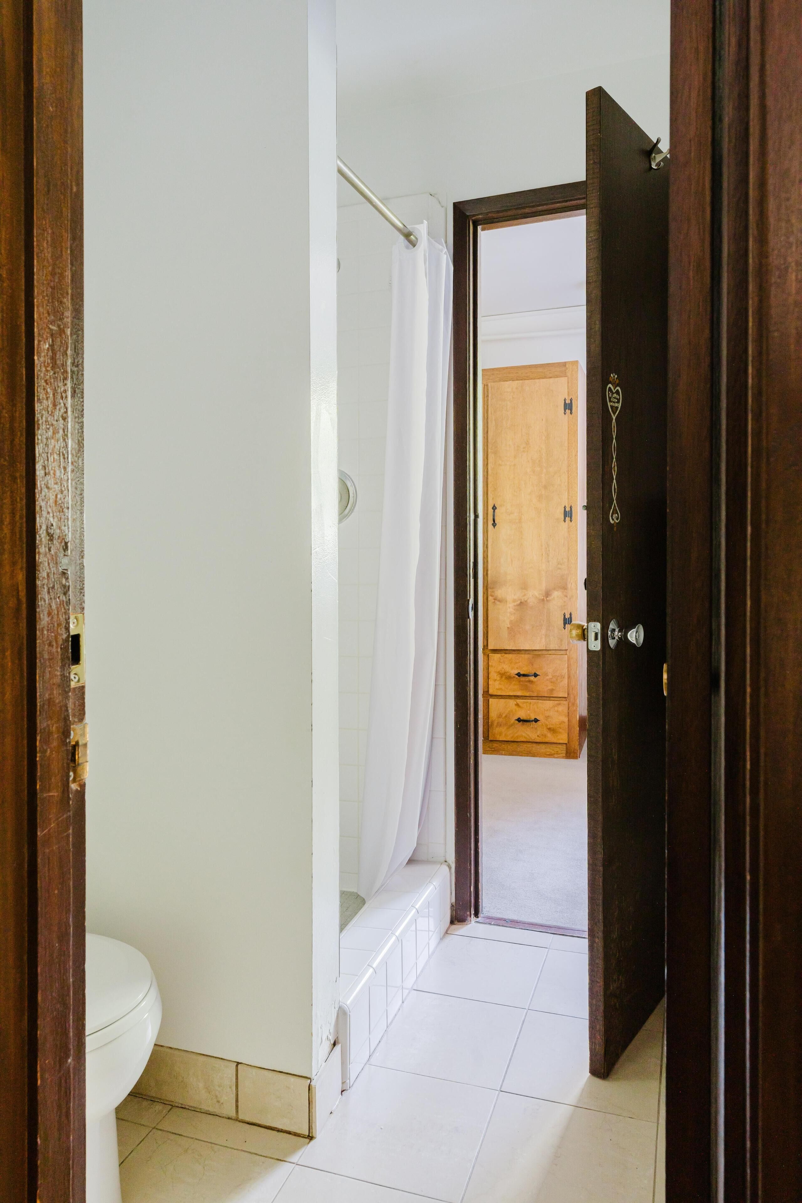 A bathroom with a toilet, shower, and wooden cabinet.