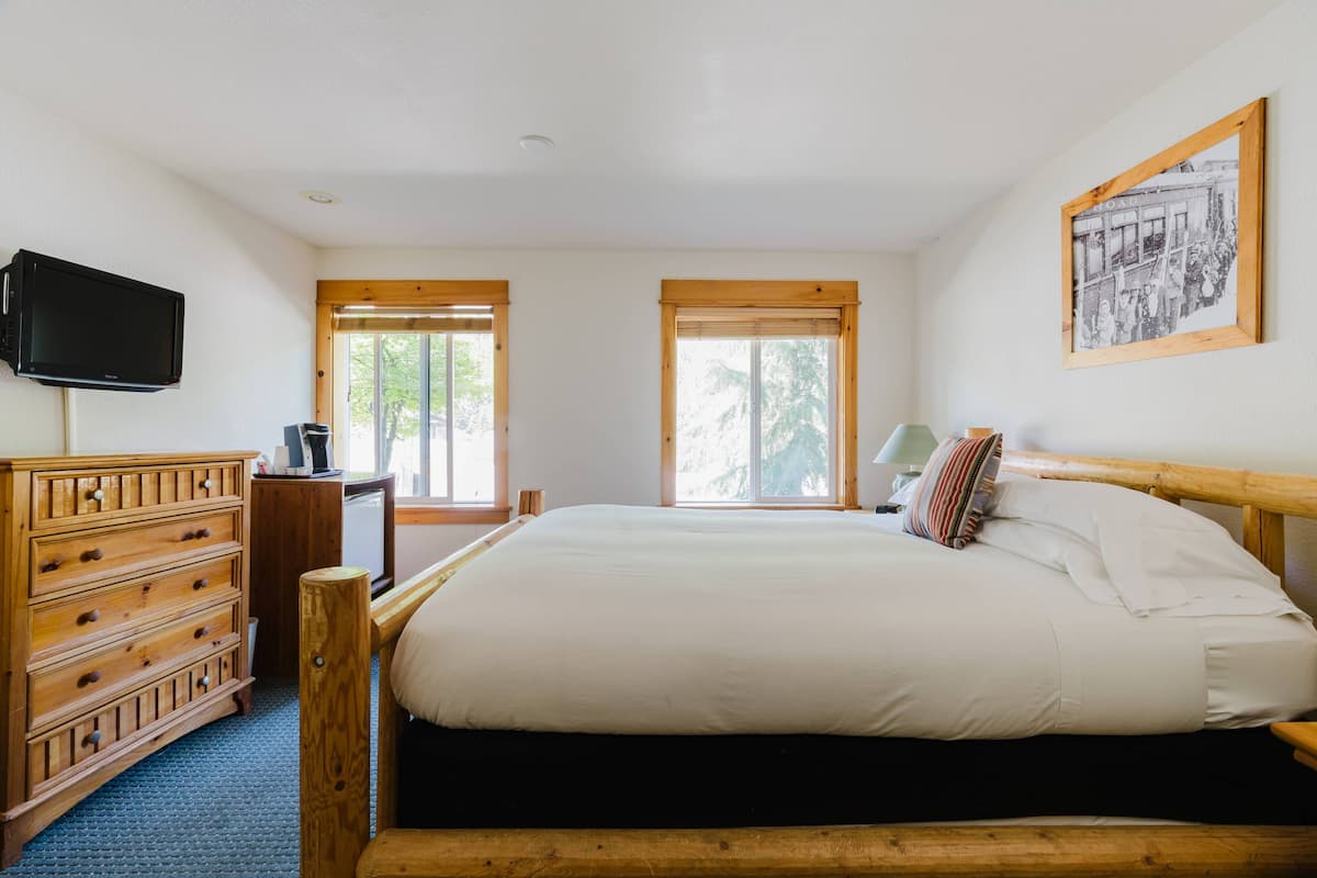 Un dormitorio con una cama de madera, un aparador, un televisor y dos ventanas.