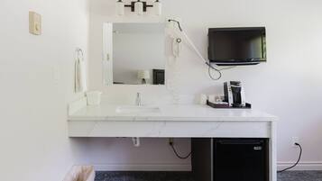 A modern bathroom with a white marble sink, a mirror, a hairdryer, a TV mounted on the wall, and a small black refrigerator.