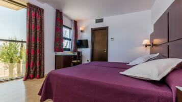 Habitación de hotel con una cama grande, un escritorio con silla, televisión y un balcón con cortinas.