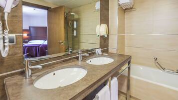 A hotel bathroom with two sinks, a large mirror, a hairdryer, and a bathtub.