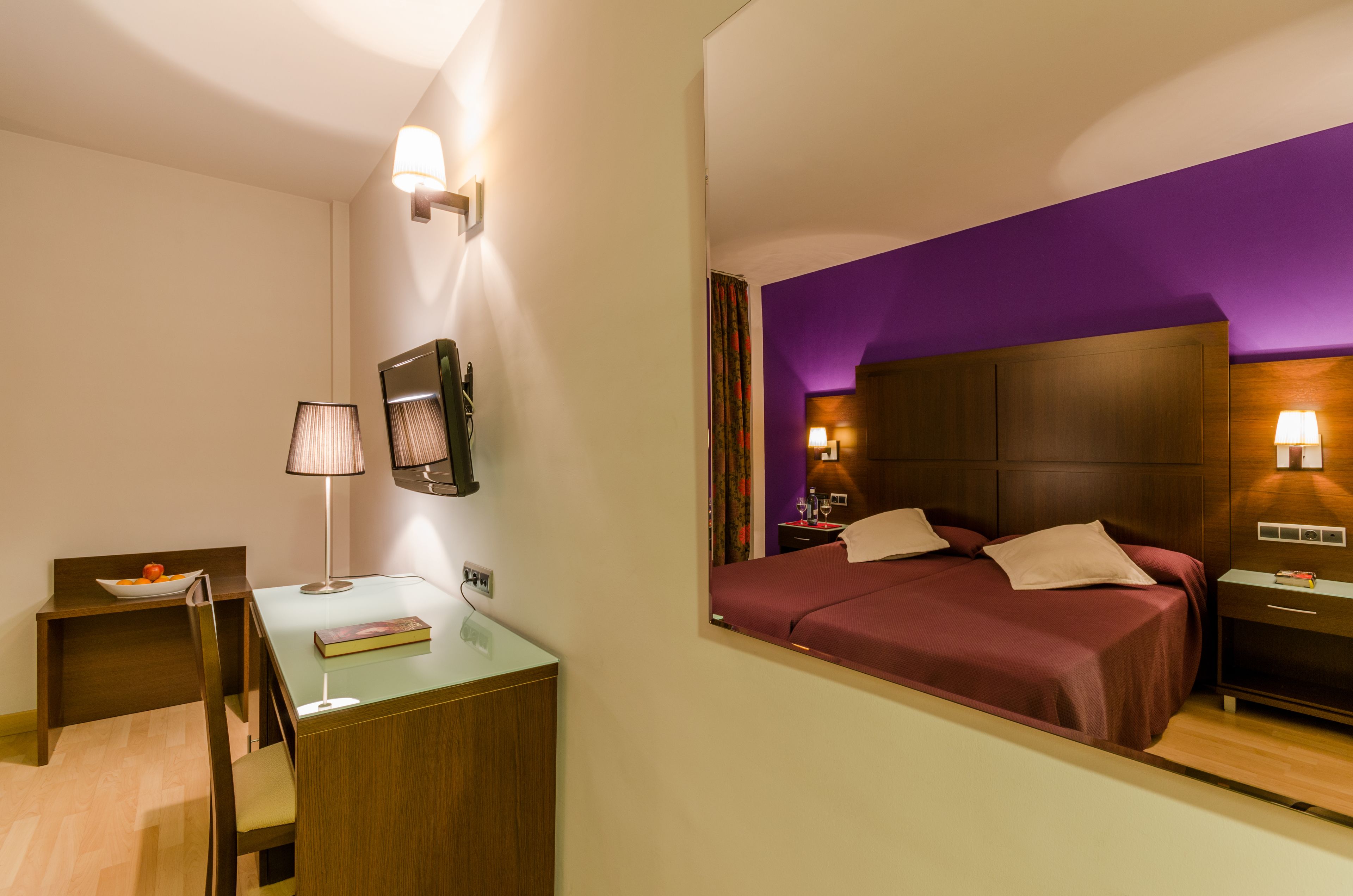 A hotel room with a bed, bedside tables, a desk, and a chair.