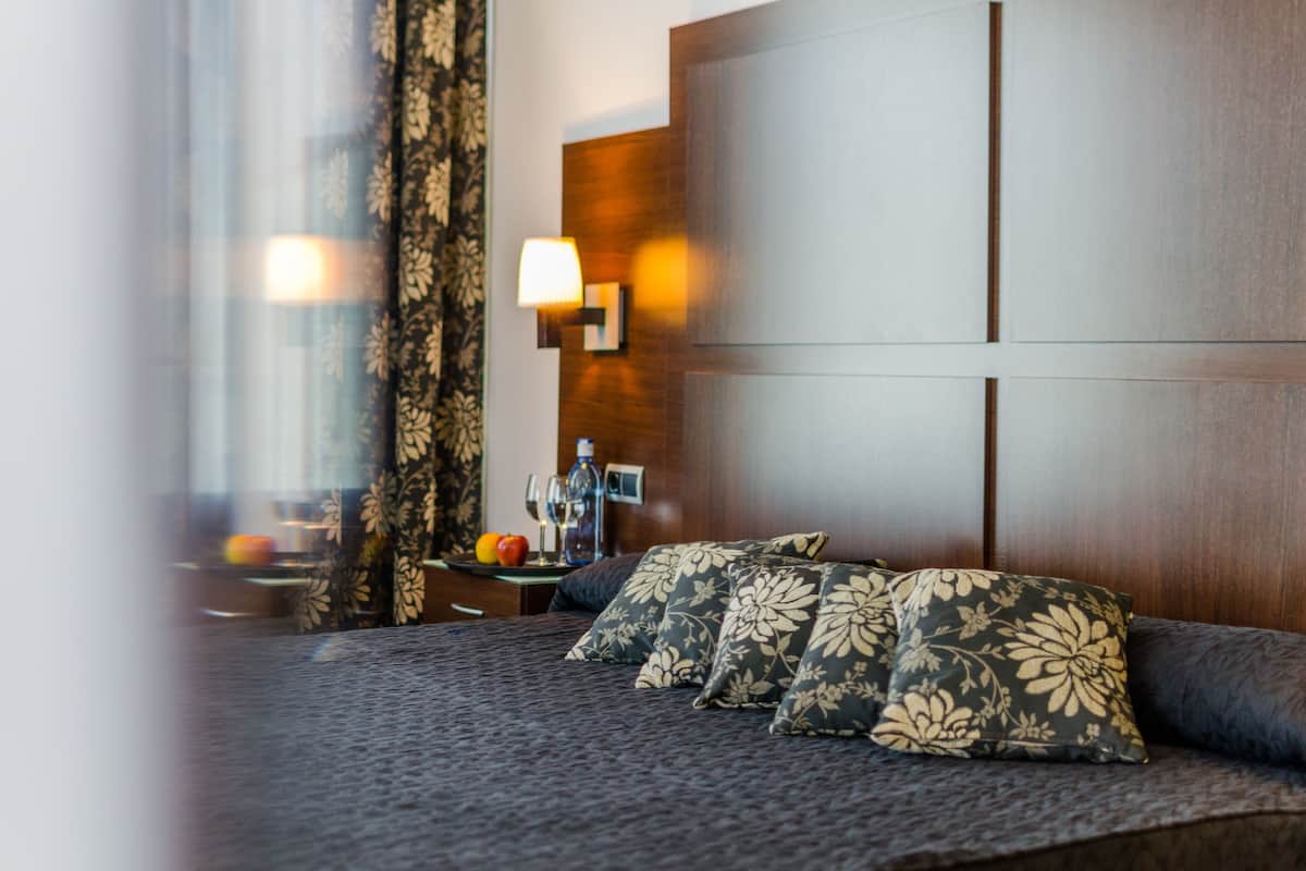 Quarto de hotel com cama, mesa de cabeceira, abajur e vista para o exterior.
