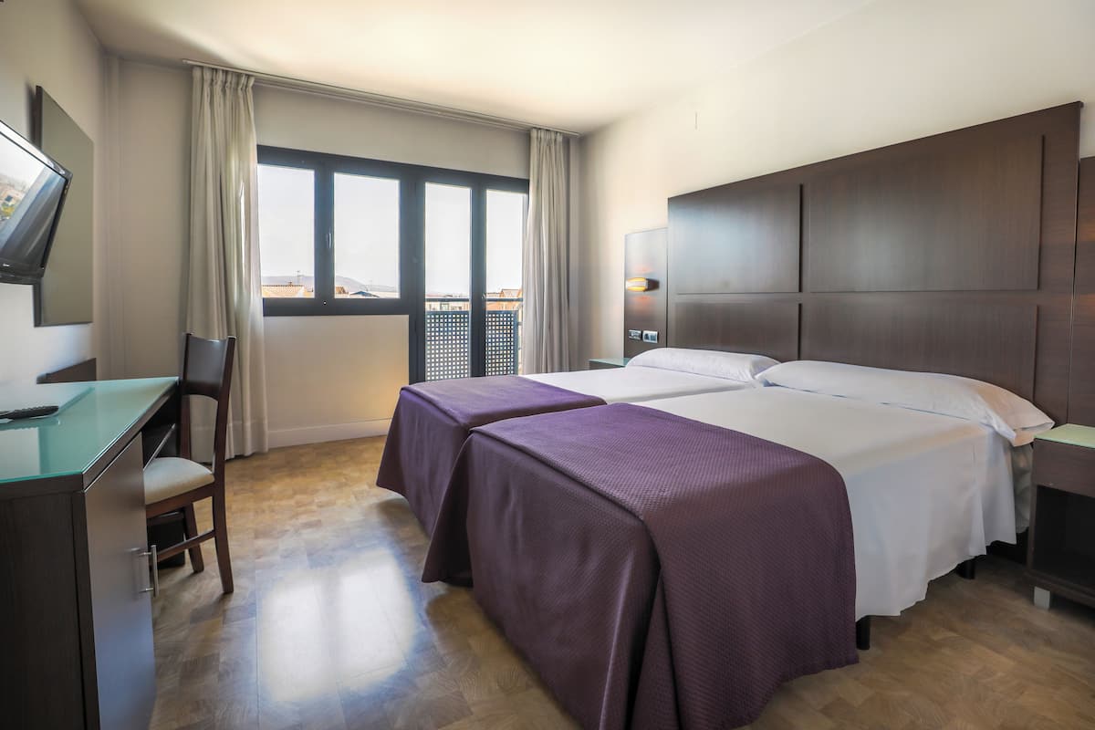 Quarto de hotel com duas camas, uma escrivaninha, uma cadeira e uma televisão.