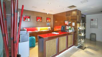 A modern hotel reception area with a wooden reception desk, a computer, and a glass display case.