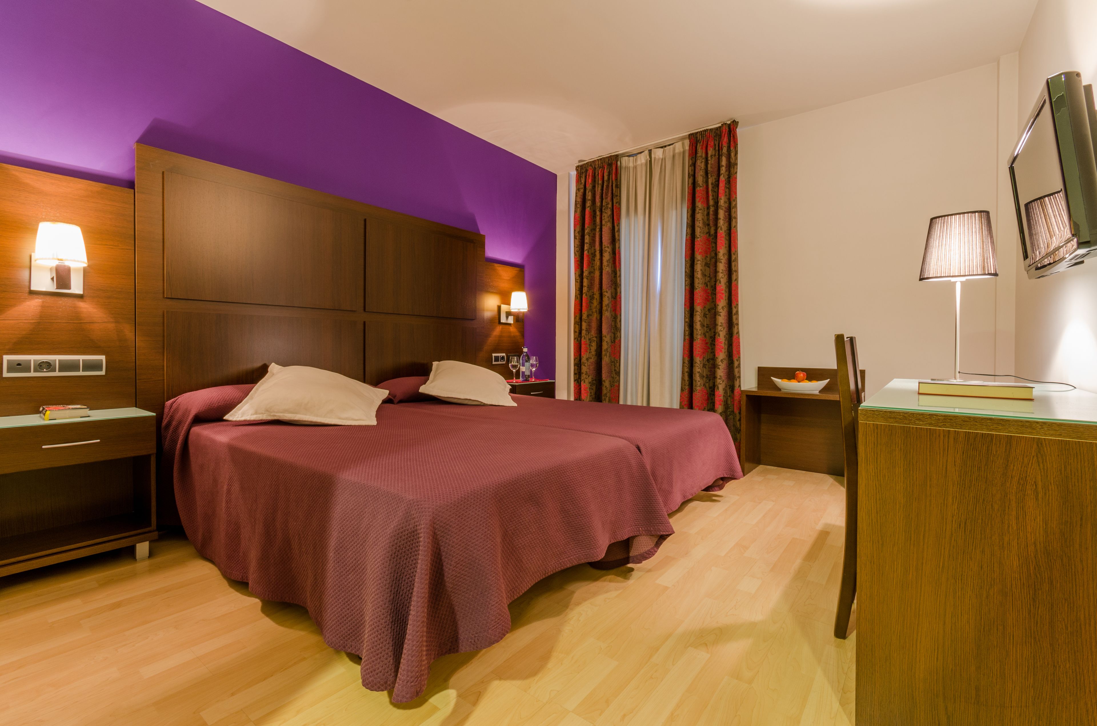 Una habitación de hotel con una cama grande, cabecera de madera, dos mesitas de noche, un escritorio y una silla.