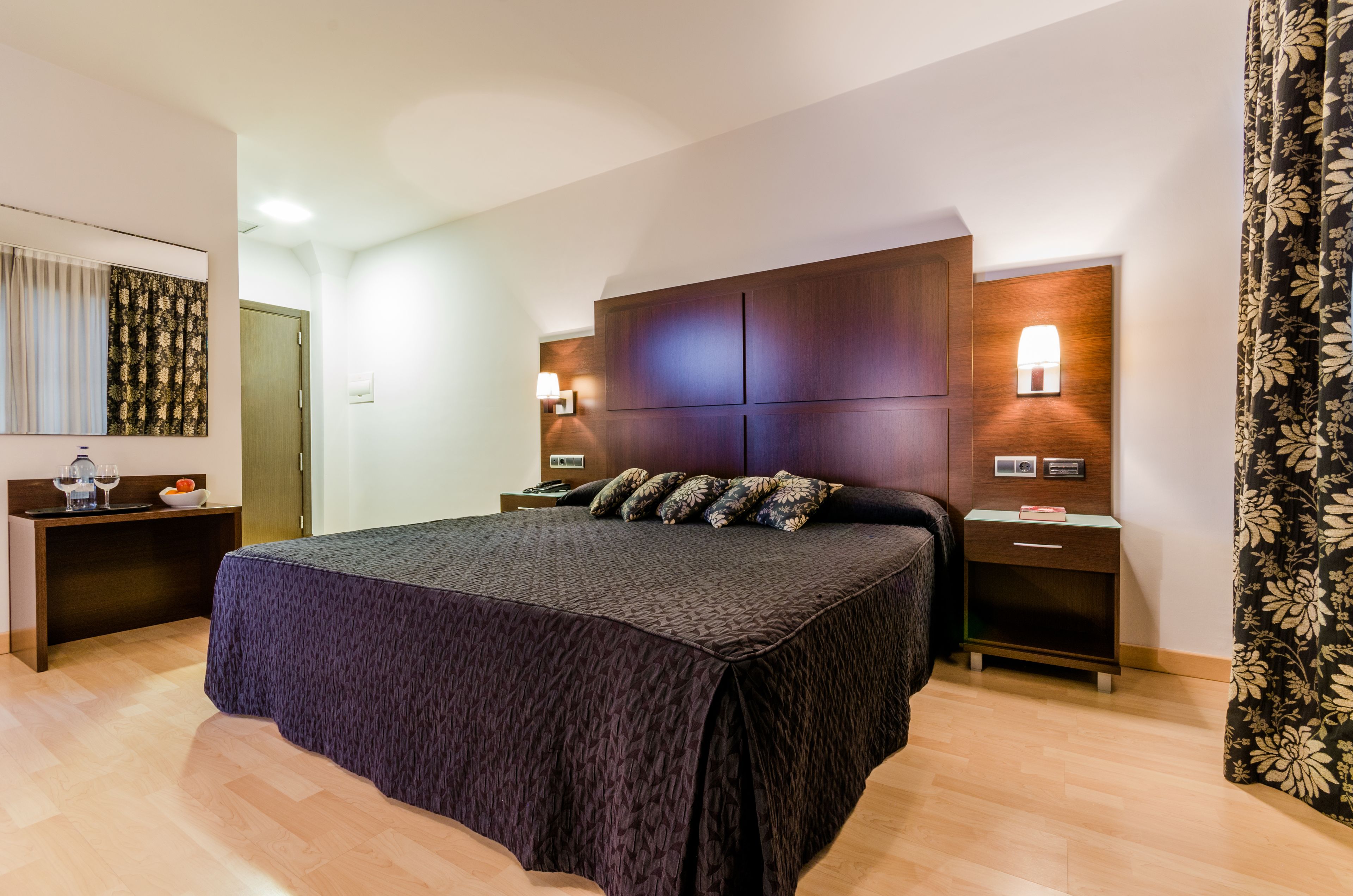Un dormitorio moderno con una cama grande, cabecera de madera, mesitas de noche y una mesita auxiliar.