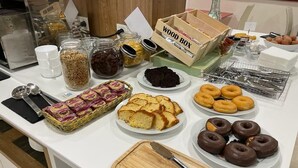 Une table de buffet proposant divers plats, notamment des gâteaux, des beignets et des pots de confitures.