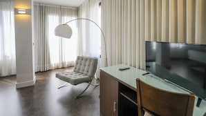 Un salon moderne avec un parquet en bois foncé, un fauteuil à capitons, une table basse en verre, un téléviseur à écran plat et un lampadaire.