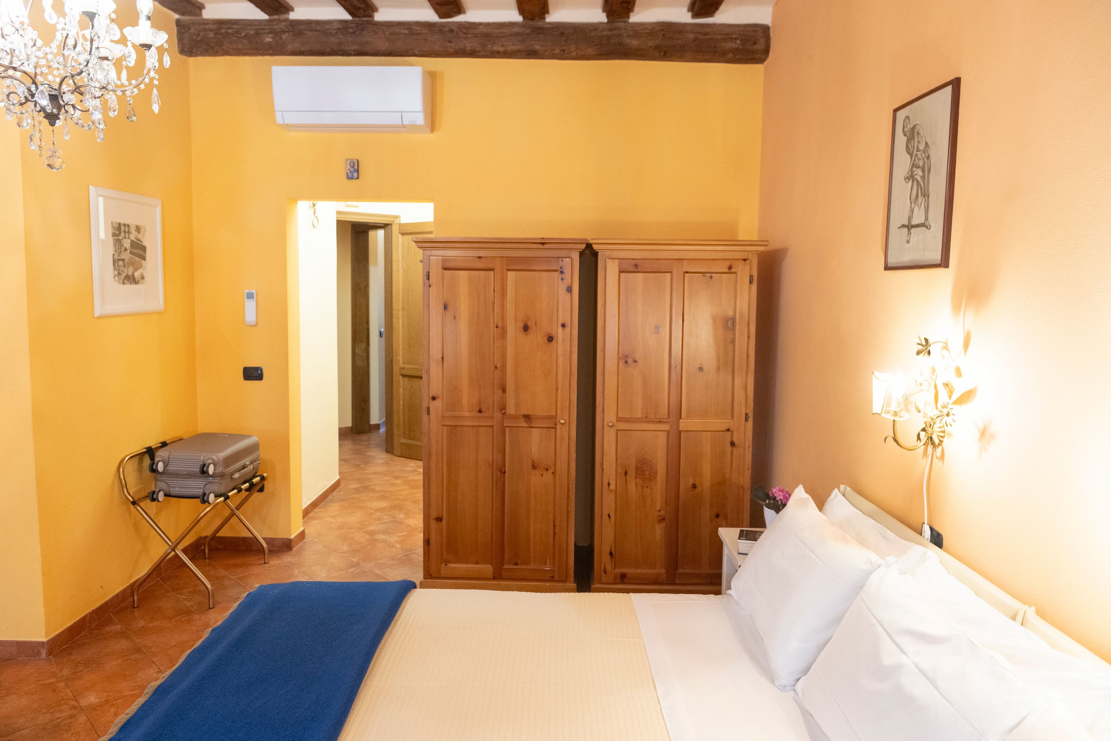 Une chambre d’hôtel avec un lit, une armoire, un lustre et une valise.