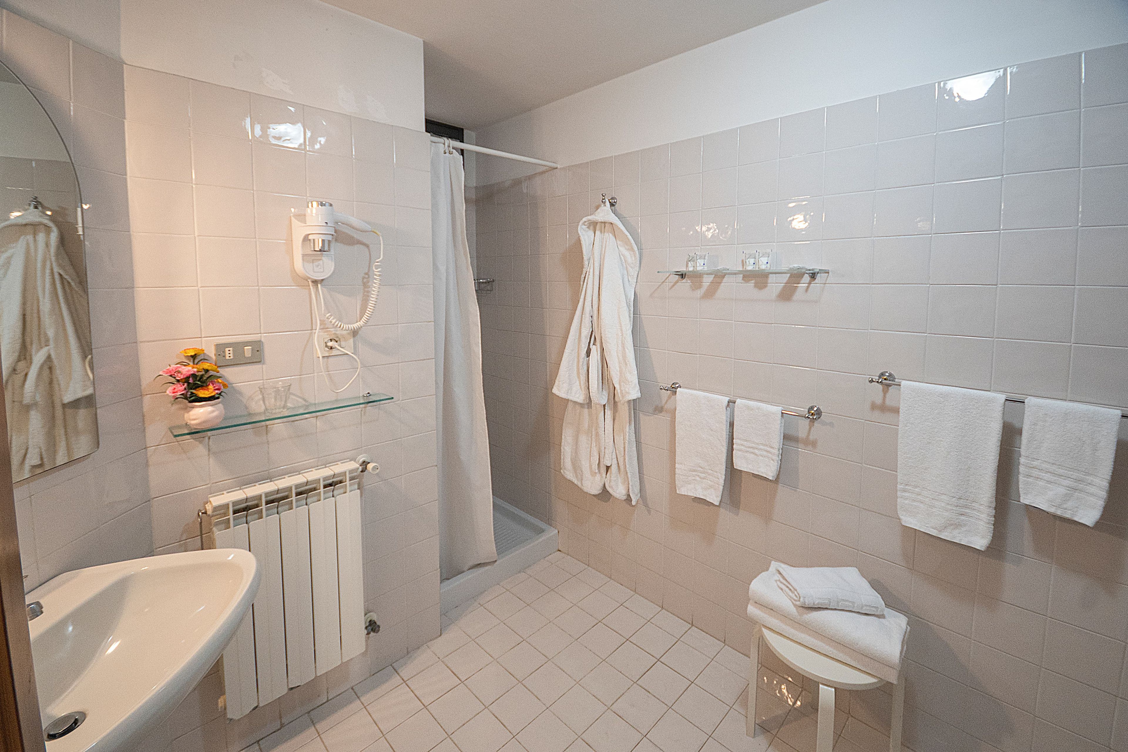 Un bagno con lavandino, cabina doccia in vetro, WC e diversi asciugamani su ganci.