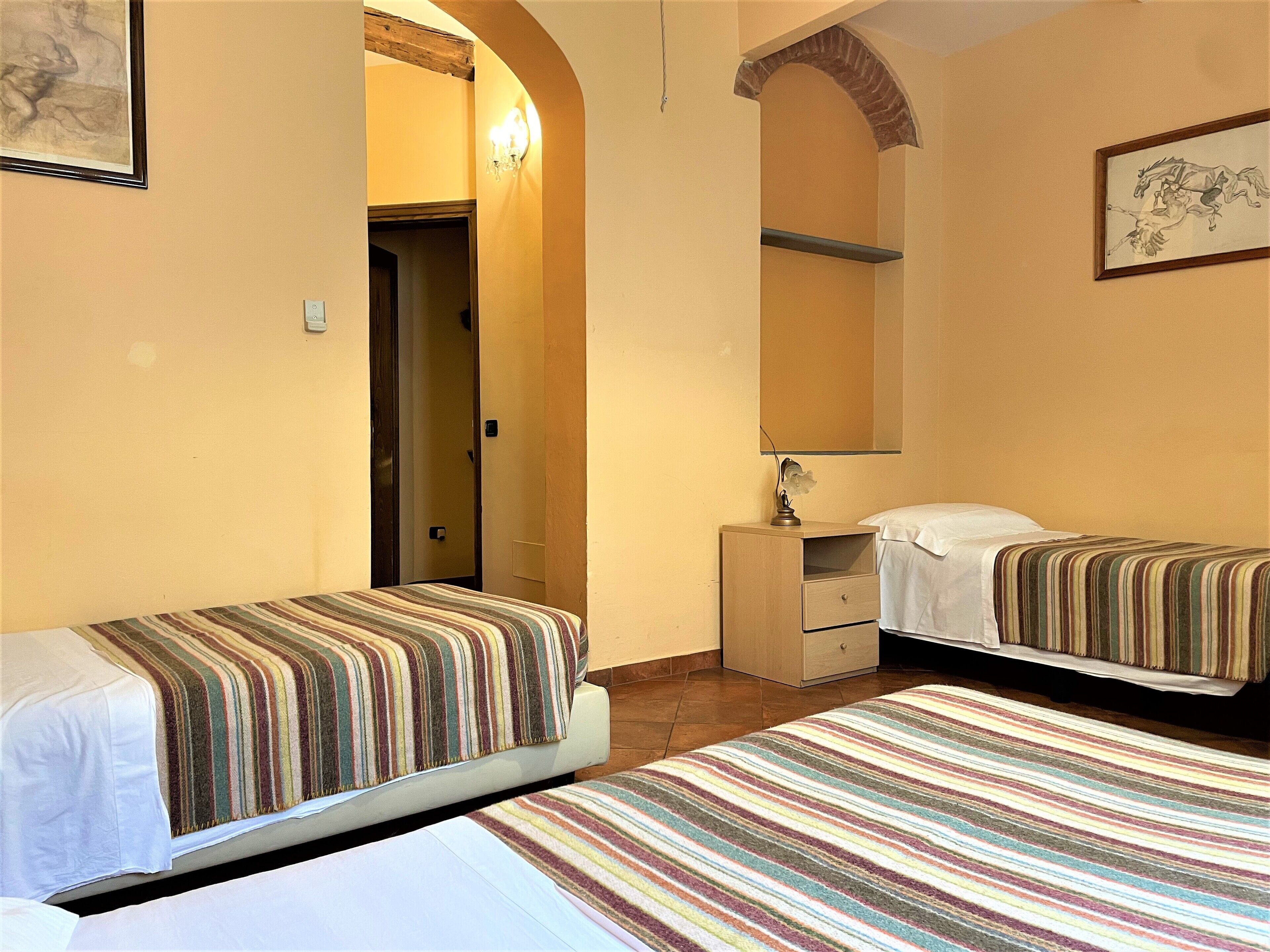 A hotel room with two beds, a small desk, a mirror, and a door leading to another room.