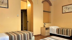 A hotel room with two beds, a small desk, a mirror, and a door leading to another room.