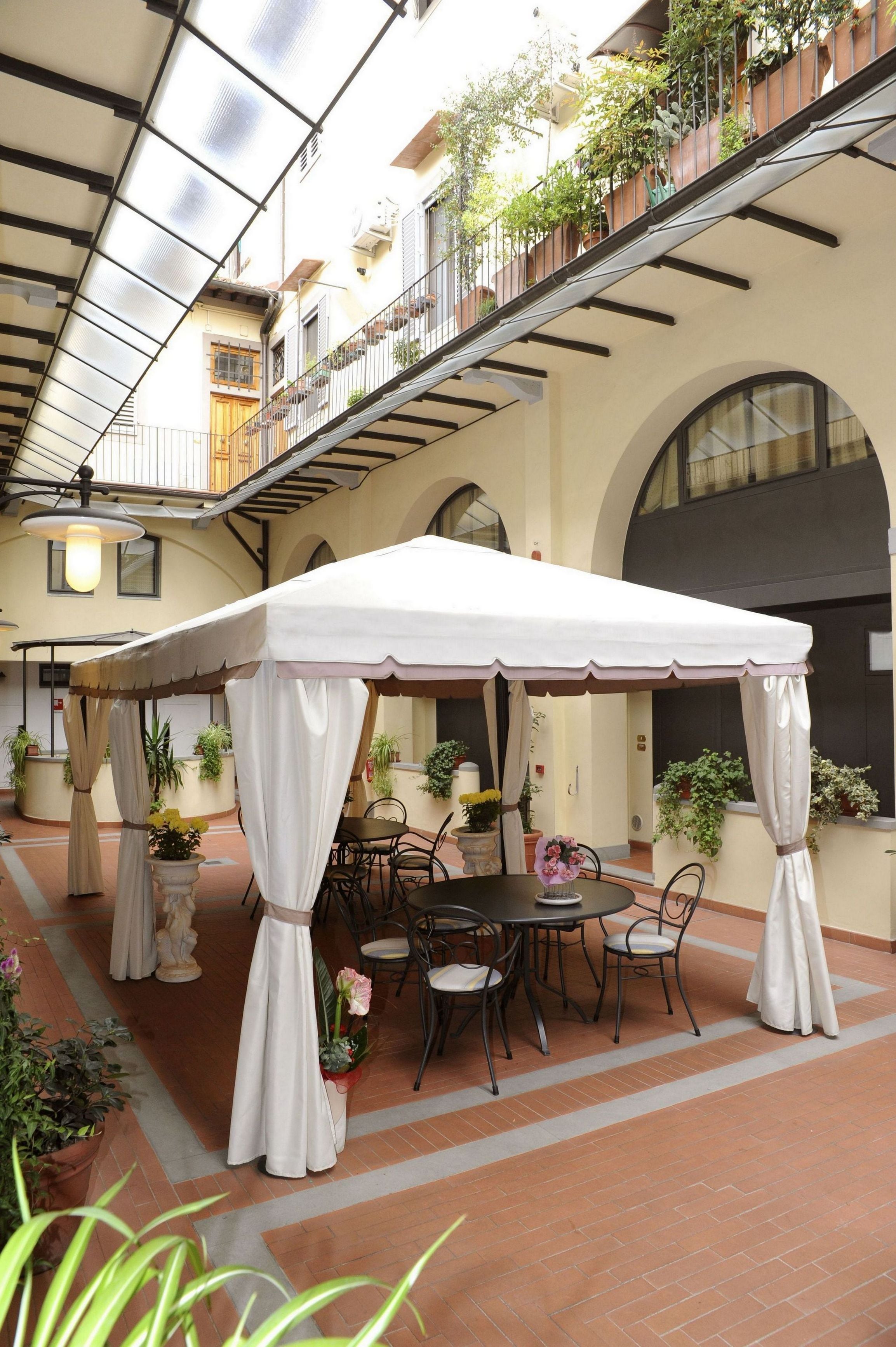 A covered outdoor seating area with a table and chairs, surrounded by potted plants and a white canopy.