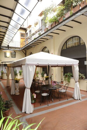 A covered outdoor seating area with a table and chairs, surrounded by potted plants and a white canopy. - Residence La Contessina (Florence)