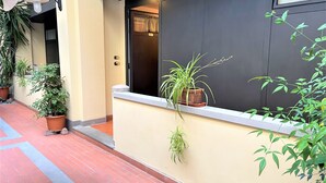A hotel corridor with potted plants, a light fixture, and a door with a number.