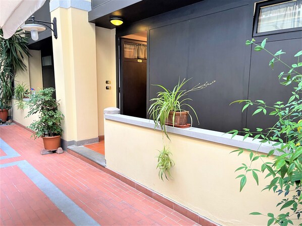 A hotel corridor with potted plants, a light fixture, and a door with a number. - Residence La Contessina (Florence)