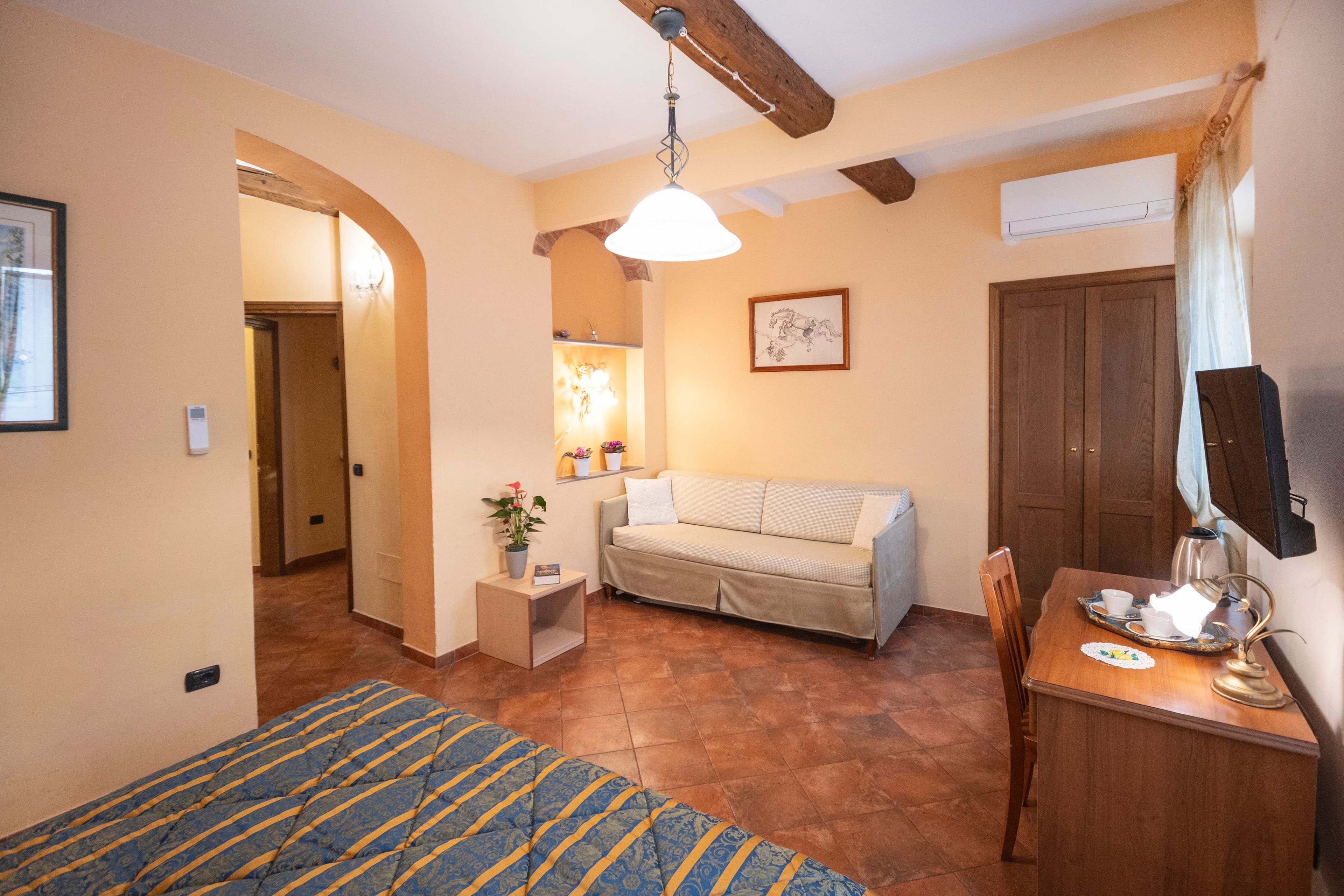 A cozy room with a bed, a sofa, a small table with a lamp, and a wooden door.