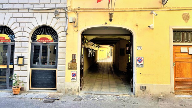 A narrow alleyway with a yellow building on the right, a blackboard with writing, and a sign indicating a car park.