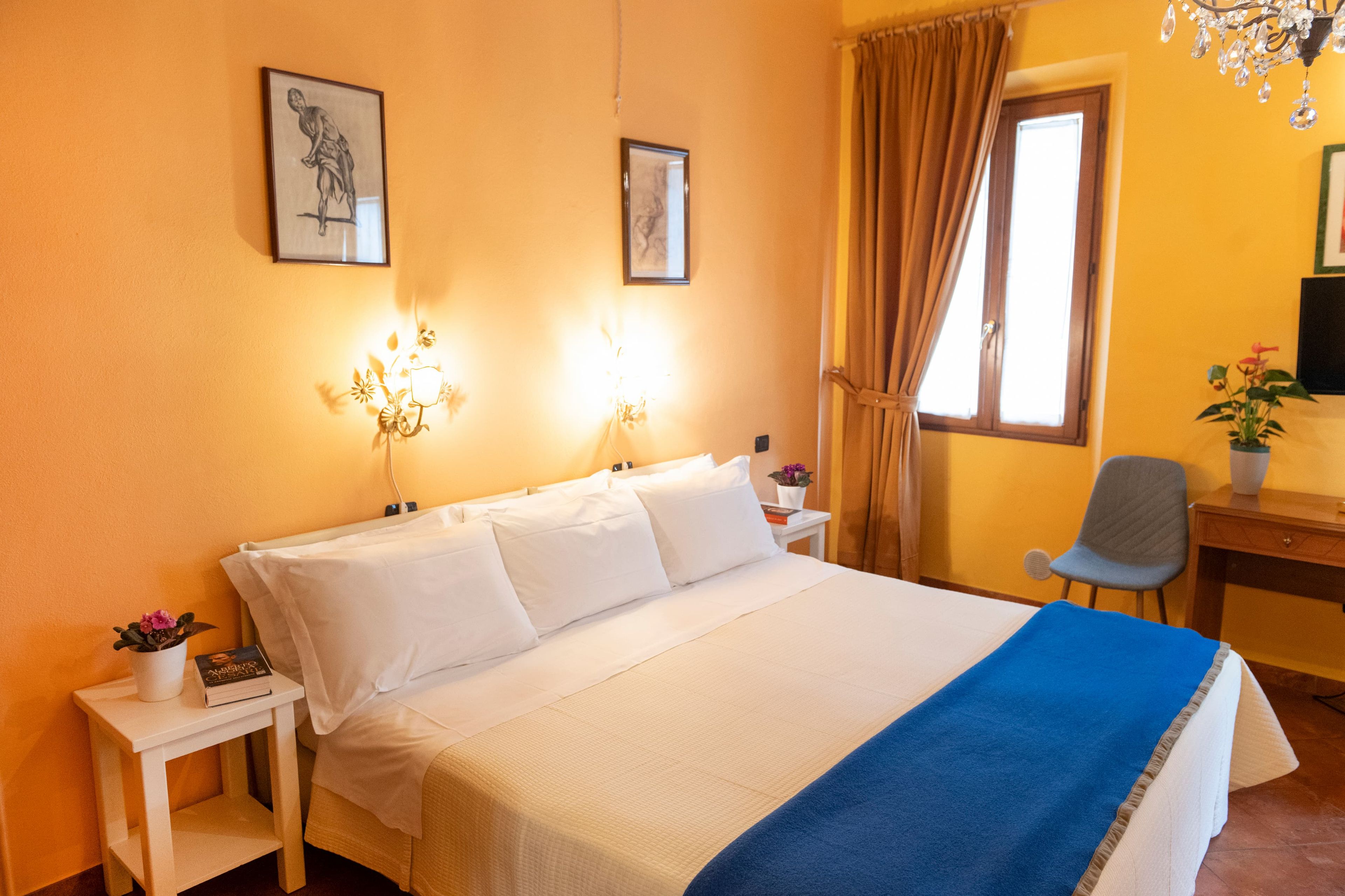 Una habitación de hotel con cama, mesitas de noche, escritorio, silla y ventana con cortinas.