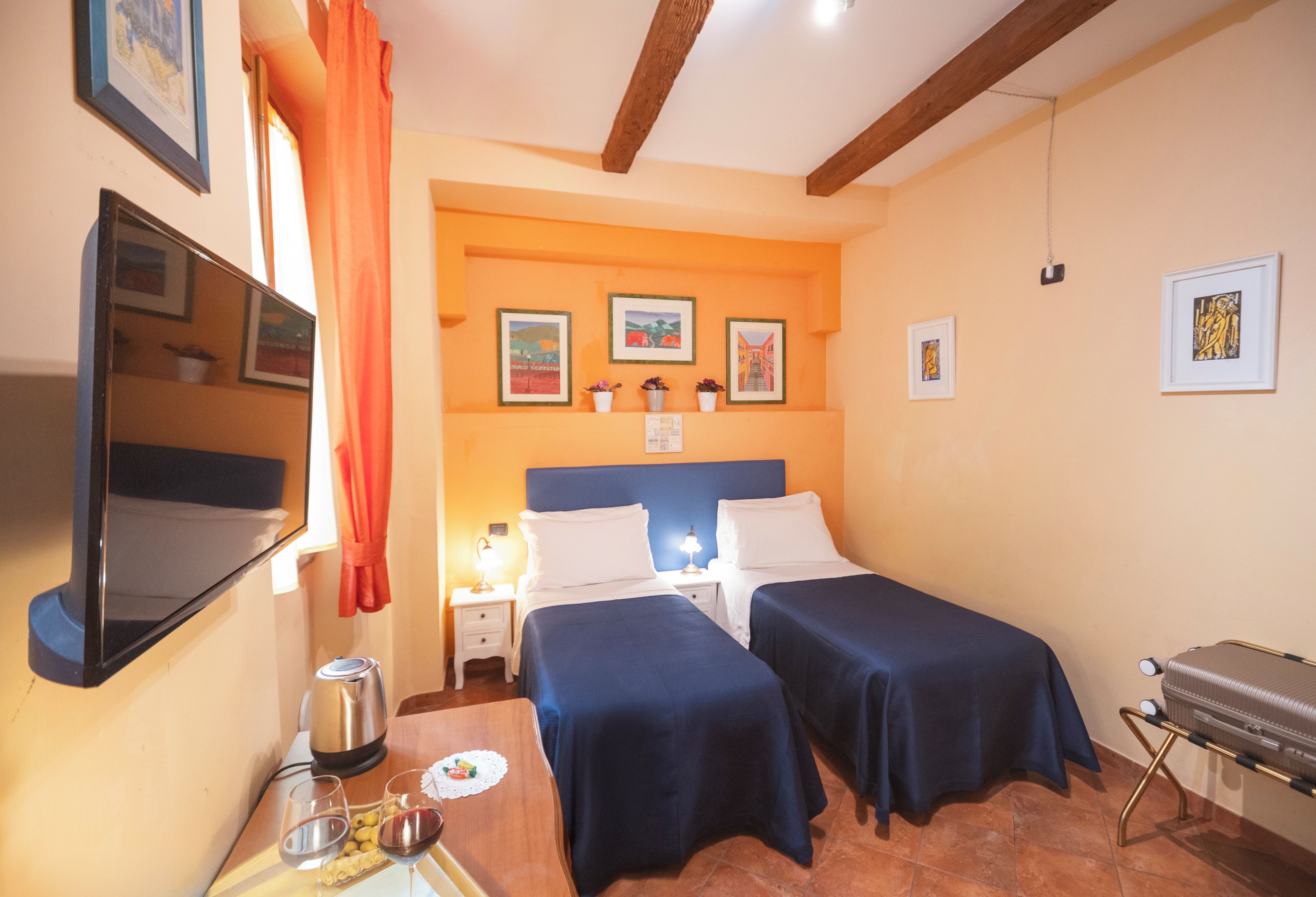 A hotel room with two beds, a TV, a minibar, and artwork on the walls.