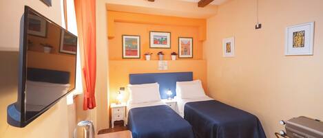 A hotel room with two beds, a TV, a minibar, and artwork on the walls.