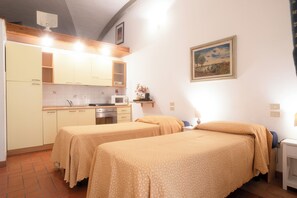 A room with two beds, a kitchenette, and a painting on the wall.