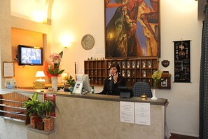A hotel reception desk with a television, a large painting, and a display of awards.