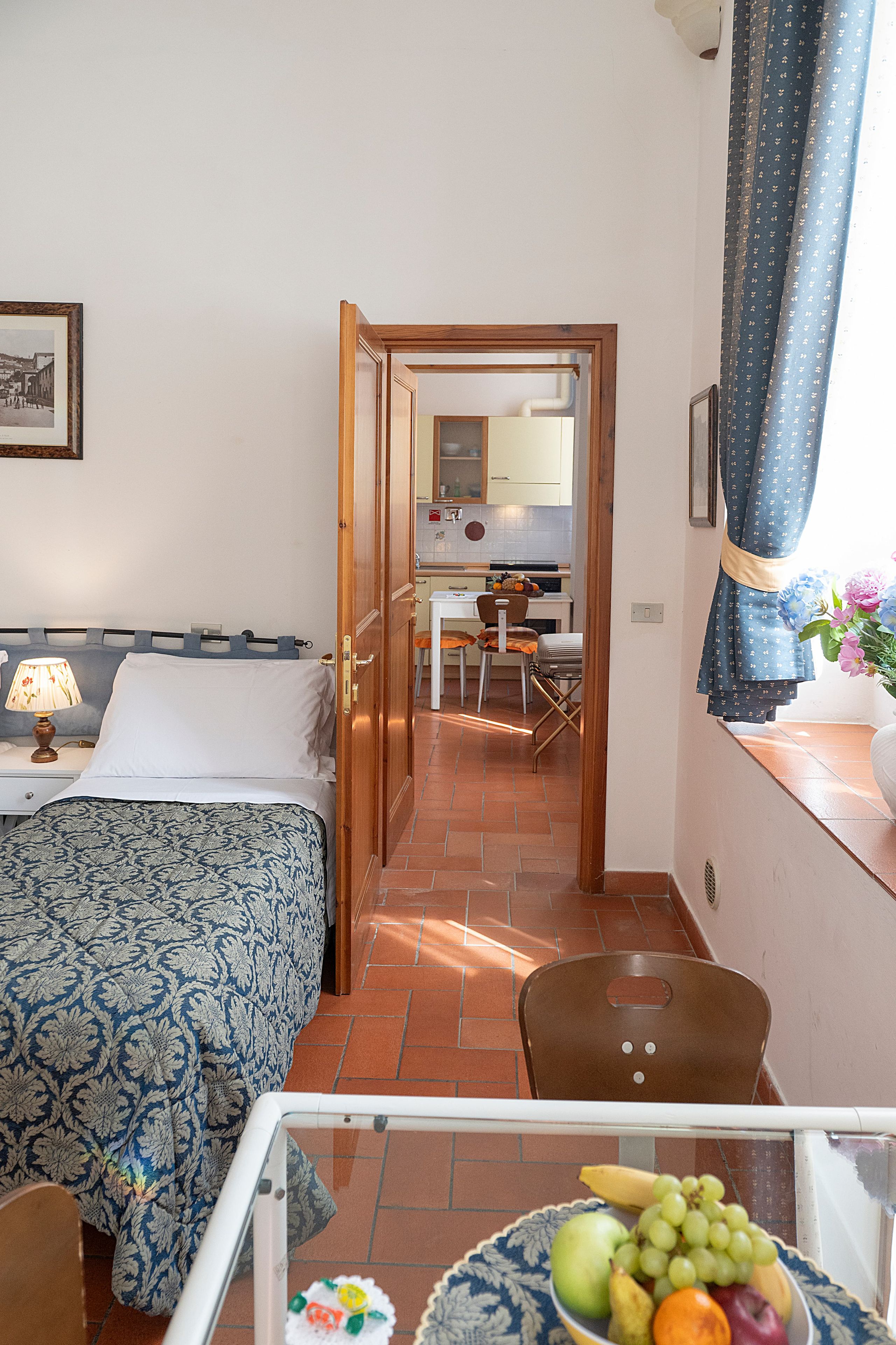 A hotel room with a bed, a desk with a chair, a small kitchen area, and a bathroom visible through an open door.